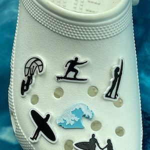 May include: White shoe with various black and blue silhouette charms of people surfing, kiteboarding, and riding waves.