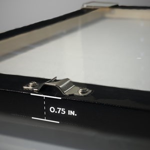 May include: Close-up of a black canvas frame with a metal hanging bracket. The frame is 0.75 inches thick.