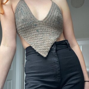 May include: A brown and green crocheted halter top with a triangular shape. The top is worn over black high-waisted pants.
