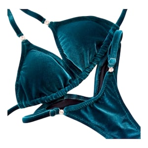 May include: A teal velvet bikini set featuring triangle cups and matching bottoms. The swimwear is accented with small, clear circular crystal embellishments on the thin straps and side connectors, providing a subtle sparkle against the soft fabric.