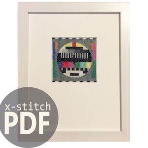 May include: A framed cross-stitch pattern of a vintage television test pattern. The pattern is in black, white, grey, red, green, blue, yellow, pink, and orange. The pattern is surrounded by a white frame.