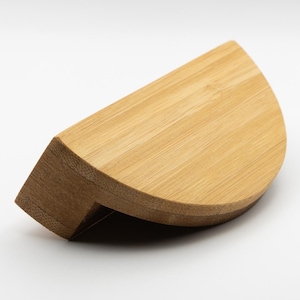 Könnte beinhalten: Ein hellbrauner, halbkreisförmiger Holz-Schrankgriff. Der Griff hat eine abgerundete Kante und eine flache Oberfläche.