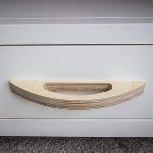 May include: A white drawer with a wooden, curved handle. The handle is made of layered plywood and has a rounded shape.