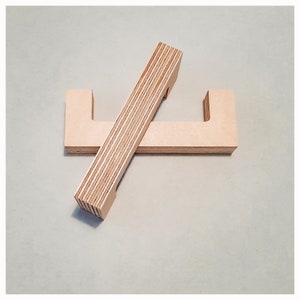 Può includere: Due maniglie in legno con un design a forma di U, realizzate in compensato stratificato. Le maniglie sono incrociate l'una sull'altra.