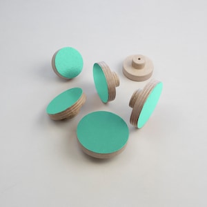 May include: Six wooden knobs with a round, flat top painted in a light turquoise colour. The knobs have a small hole in the centre for attaching to a surface.