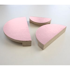 Könnte beinhalten: Drei rosafarbene, halbkreisförmige Holzregale in verschiedenen Größen. Die Regale sind aus Sperrholz gefertigt und haben eine glatte, polierte Oberfläche.