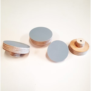May include: Four light grey round wooden knobs with a natural wood finish. The knobs are made of plywood and have a smooth surface.