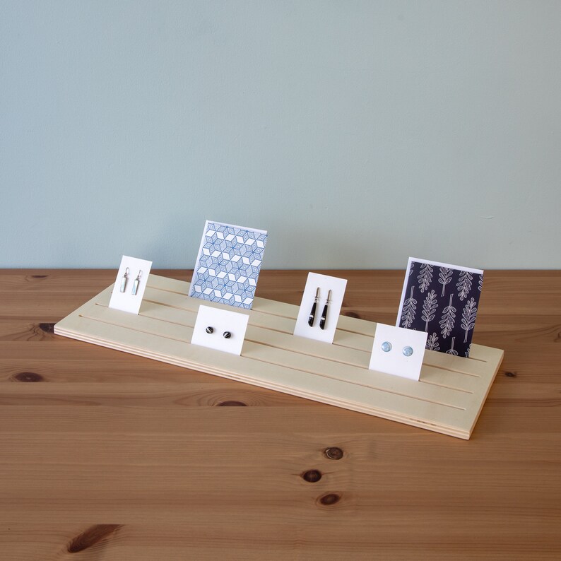 Pu&ograve; includere: Un espositore in legno con cinque fessure per esporre orecchini e carte. L'espositore &egrave; in legno chiaro e ha una finitura naturale. Le carte hanno diversi motivi, tra cui disegni geometrici e floreali. Gli orecchini sono argentati e neri.