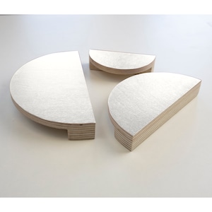 Puede incluir: Tres estantes de madera en forma de semicírculo de diferentes tamaños. Los estantes están hechos de madera clara con un patrón de veta natural.