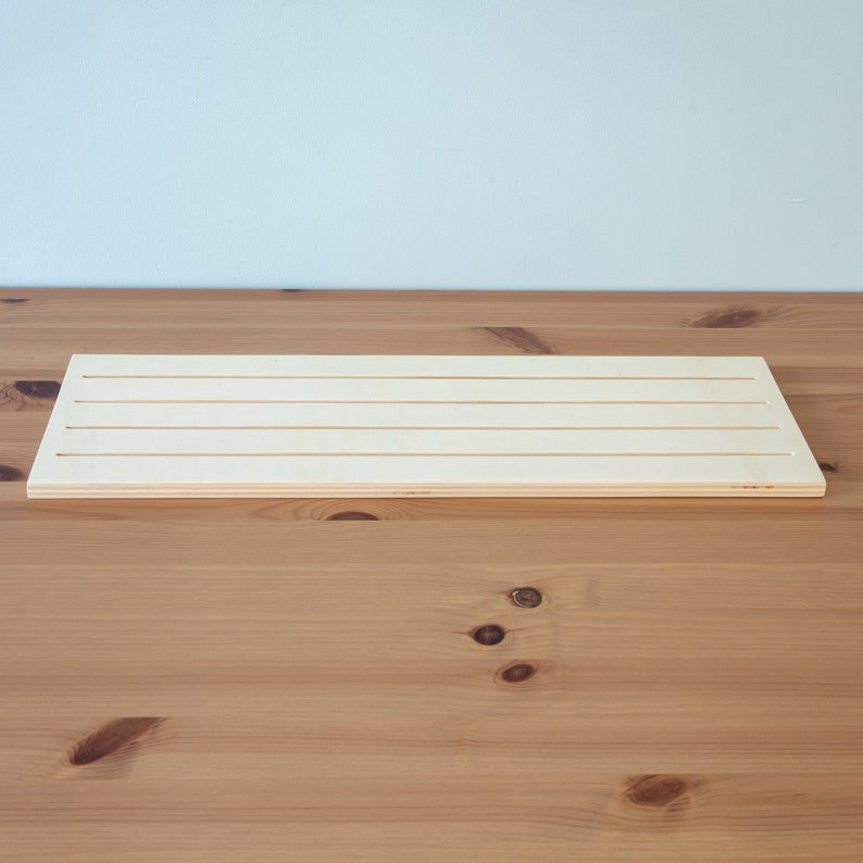 Pu&ograve; includere: Un tagliere di legno bianco con quattro scanalature parallele che corrono per tutta la lunghezza del tagliere.