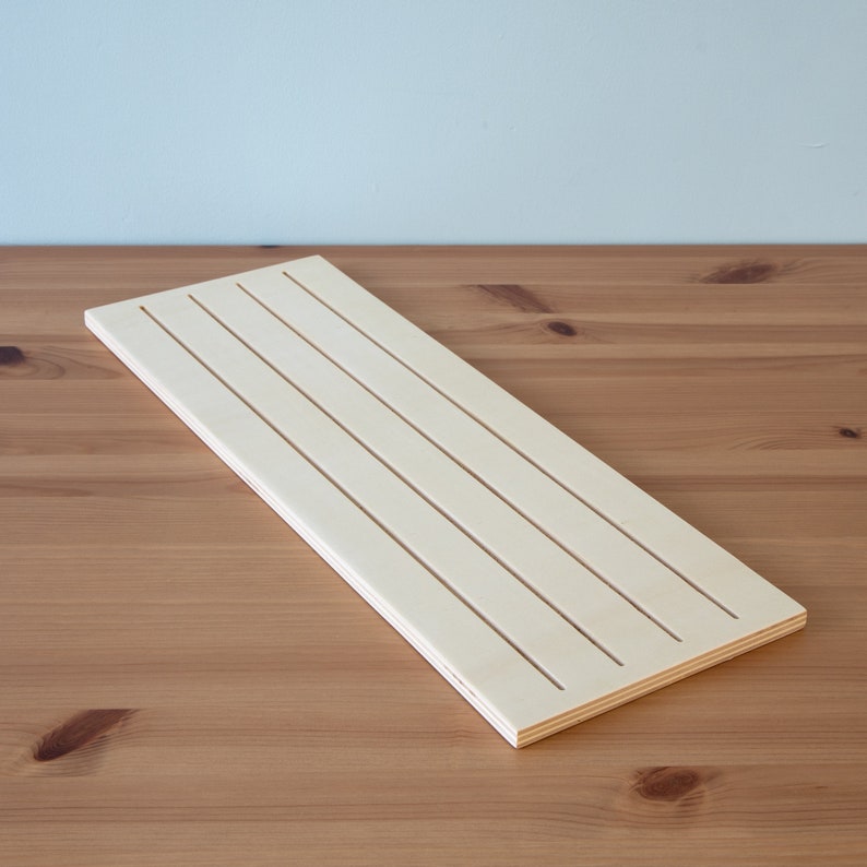 Pu&ograve; includere: Un pezzo rettangolare di legno grezzo di colore chiaro con cinque scanalature parallele tagliate nella superficie.