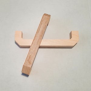 Op de afbeelding: Twee houten handvatten met een eenvoudig, modern ontwerp. De handvatten zijn gemaakt van lichtgekleurd multiplex en hebben een licht gebogen vorm.