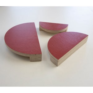 Può includere: Tre pomelli per armadi in legno rosso a forma di semicerchi. I pomelli sono in compensato e hanno una finitura liscia rossa.