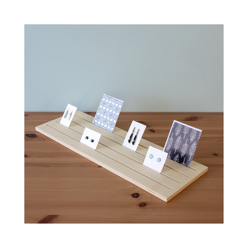 Pu&ograve; includere: Un espositore in legno con quattro fessure per esporre orecchini e carte. L'espositore &egrave; in legno chiaro e ha una finitura naturale. Le carte sono bianche con diversi motivi e design. Gli orecchini sono neri e blu.