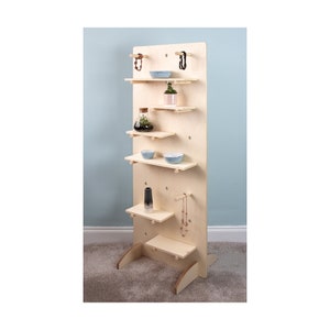 May include: A light wood wall shelf unit with five shelves and multiple peg holes. The shelves are decorated with small plants, bowls, and vases.