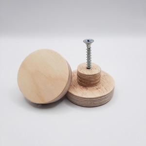 Pode incluir: Dois botões de madeira com um parafuso no centro. Os botões são feitos de madeira clara e têm uma forma redonda.