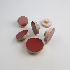 Könnte beinhalten: Sechs runde Holzgriffe mit einer roten lackierten Oberseite. Die Griffe sind aus Sperrholz und haben eine natürliche Holzoptik an den Seiten.