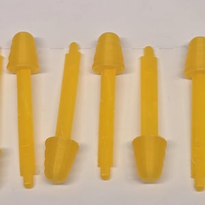 May include: Several yellow plastic objects with a cylindrical stem and a conical top are arranged in a row. The objects have a uniform color and appear to be small tools or components.