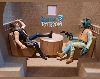 May include: Two action figures, Han Solo and a blue alien, are sitting in chairs around a small wooden table. The scene is set in a brown and beige room with a sign that reads "Brad's Toy Room".