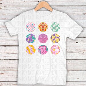 May include: A white t-shirt with a design of nine colorful basketballs with different patterns. The basketballs are arranged in three rows of three.
