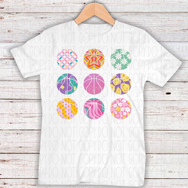 May include: A white t-shirt with a design of nine colorful basketballs with different patterns. The basketballs are arranged in three rows of three.