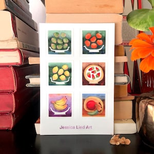 Puede incluir: Una impresión artística blanca con seis ilustraciones en acuarela de frutas en cuencos. Las frutas incluyen aceitunas verdes, tomates rojos, limones amarillos, fresas, plátanos y una manzana roja. El nombre del artista, "Jessica Lied Art", está impreso en la parte inferior.
