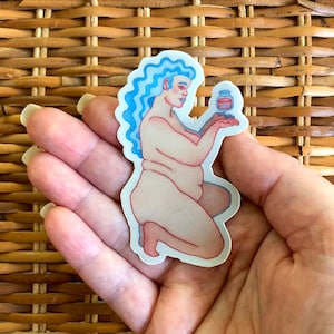 Puede incluir: Una pegatina que representa una figura desnuda con cabello azul y contornos rojos, sosteniendo un pequeño frasco. La figura está arrodillada, con un tono de piel claro. La pegatina tiene un borde blanco y se sostiene en una mano.