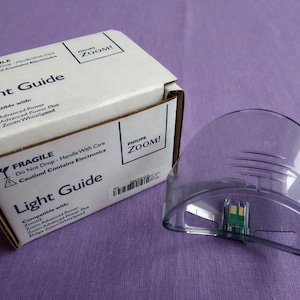Könnte beinhalten: Ein klarer Lichtleiter aus Kunststoff mit gebogenem Design, neben einer weißen Box. Auf der Box steht "Light Guide" und "Philips ZOOM!", sowie Warnhinweise auf zerbrechliche Elektronik.