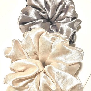 May include: Three satin scrunchies in different shades of gray, beige, and white. The scrunchies are made of soft, silky fabric and are perfect for holding hair in place.