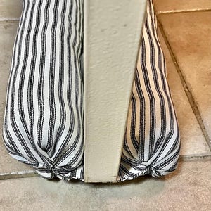 May include: Two white and black striped door draft stoppers are placed at the bottom of a white door.