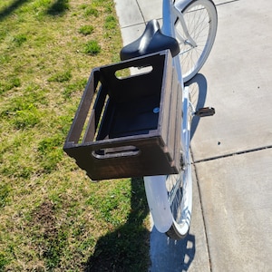 Pode incluir: Uma bicicleta branca com uma caixa de madeira presa ao porta-bagagem traseiro. A caixa est&aacute; vazia e tem uma mancha marrom escura.