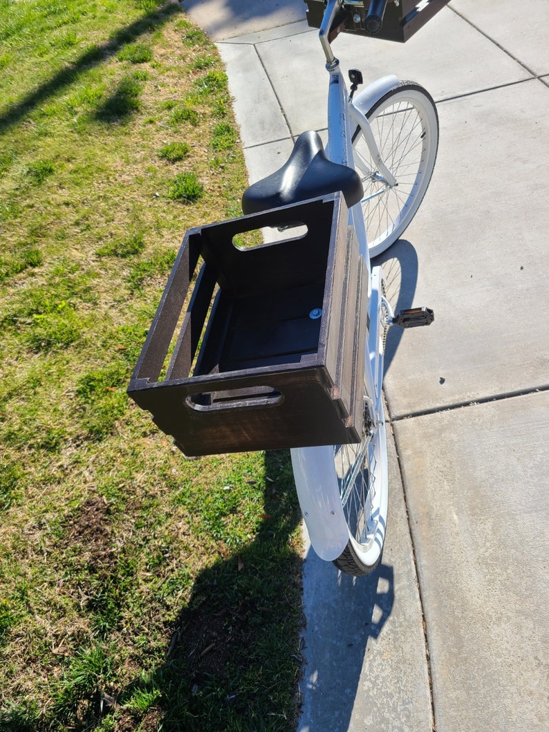 Pode incluir: Uma bicicleta branca com uma caixa de madeira presa ao porta-bagagem traseiro. A caixa est&aacute; vazia e tem uma mancha marrom escura.