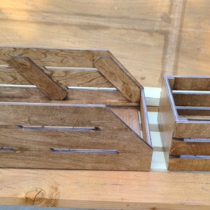 May include: Two wooden crates, one larger than the other, both with a brown stain finish. The larger crate has a slanted front and a handle on the side. The smaller crate has a rectangular shape and a handle on the side.