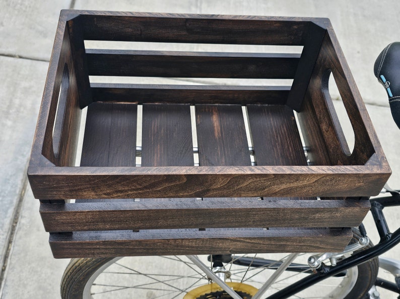 Pode incluir: Uma caixa de madeira marrom escura com duas al&ccedil;as nas laterais. A caixa est&aacute; presa a uma bicicleta.