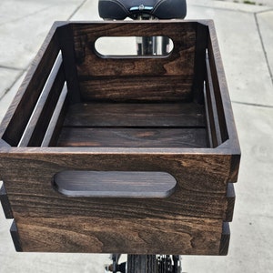 Pode incluir: Uma caixa de madeira castanho escuro com duas al&ccedil;as recortadas na frente e nas laterais. A caixa est&aacute; montada numa bicicleta.