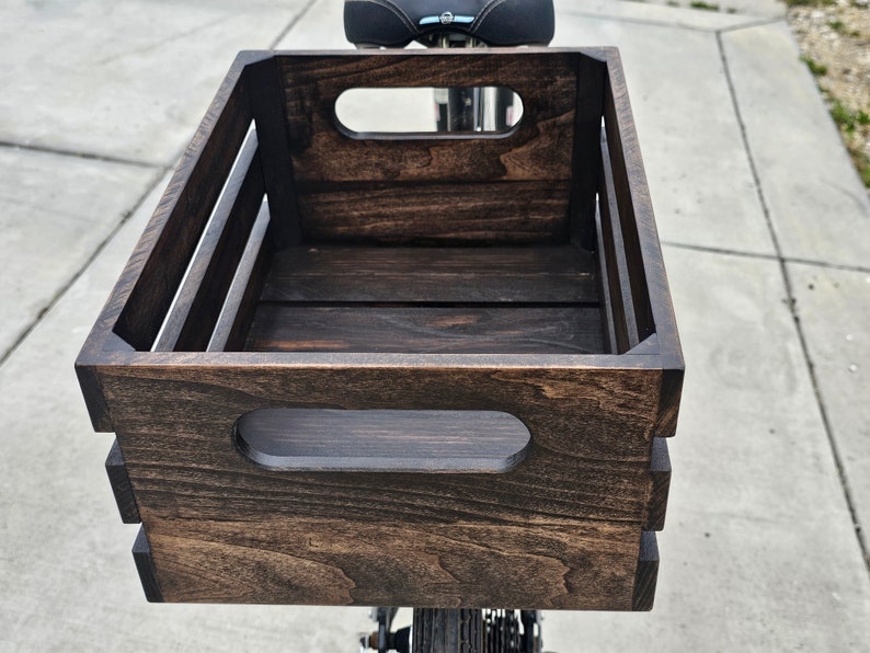 Pode incluir: Uma caixa de madeira castanho escuro com duas al&ccedil;as recortadas na frente e nas laterais. A caixa est&aacute; montada numa bicicleta.