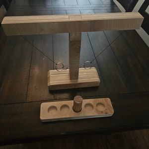May include: Wooden ring toss game with a wooden base and a wooden platform with four holes. The game is set up on a wooden table.