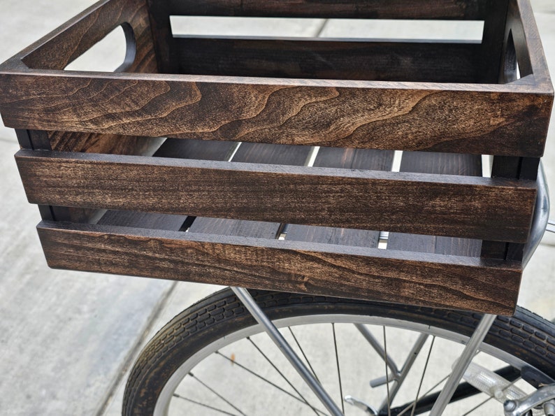 Pode incluir: Uma caixa de madeira marrom escura com um suporte de bicicleta de metal preso na parte de tr&aacute;s. A caixa est&aacute; montada em uma bicicleta.