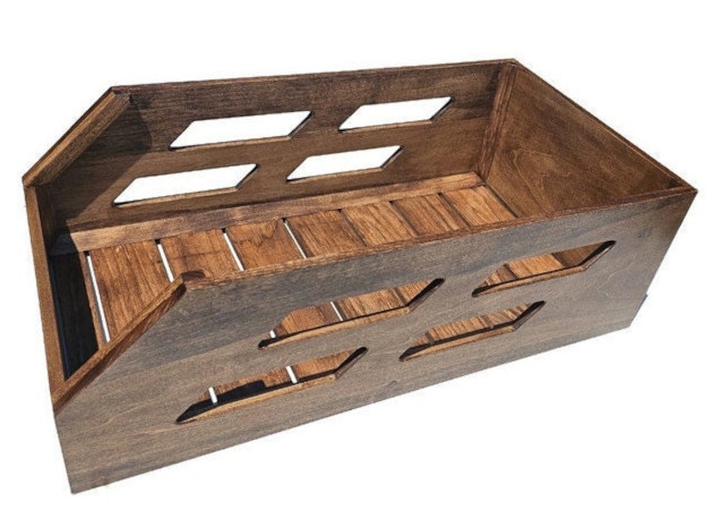 May include: A dark brown wooden crate with a rectangular shape and open sides. The crate has a series of rectangular cutouts on the front and sides, and a slatted bottom.