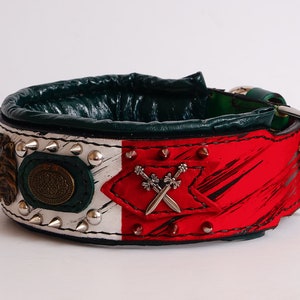 May include: A green, white, and red leather dog collar with silver studs and a metal buckle. The collar has a decorative design with a lion's head, a circular emblem, and crossed swords.