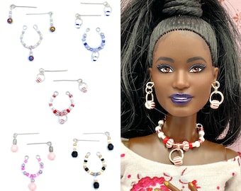 May include: Set of four pairs of doll-sized earrings with a variety of colors and designs. Each pair features a hoop with beads and a dangling charm. The earrings are made with silver-toned metal and colorful beads.