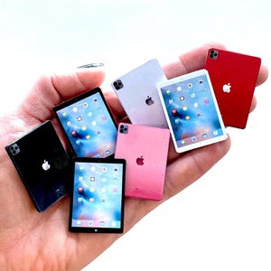May include: A collection of miniature tablets in various colors, including black, red, pink, and white. Each tablet features a screen displaying a digital interface and the Apple logo.