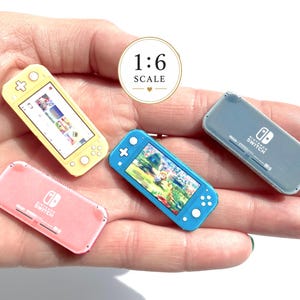 Könnte beinhalten: Vier Nintendo Switch Spielkonsolen im Miniaturformat im Maßstab 1:6 in Gelb, Blau, Pink und Grau. Die gelben und blauen Einheiten zeigen aktive Spielbildschirme, während die pinken und grauen Einheiten die Rückseite mit dem Nintendo Switch Logo zeigen.