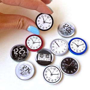 Può includere: Una collezione di piccoli orologi e display digitali dell'ora. Gli orologi analogici hanno quadranti bianchi con numeri e lancette nere, mentre gli orologi digitali mostrano l'ora, la data e la temperatura. Un orologio è tenuto in mano.