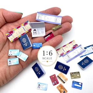 Puede incluir: Una colección de accesorios de viaje en miniatura a escala 1:6, que incluye pasaportes azules pequeños, varias tarjetas de crédito y tarjetas de embarque con patrones coloridos. Los artículos presentan texto y gráficos impresos en una palma.