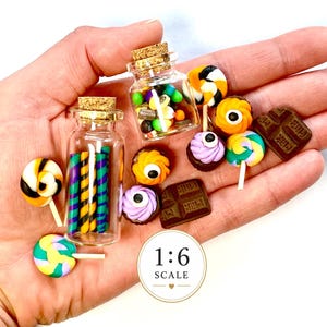 May include: Two miniature clear glass bottles with cork stoppers containing colourful candy sticks, surrounded by loose miniature sweets including lollipops, chocolate bars, and eye-themed treats. A circular label displays the text 1:6 SCALE.