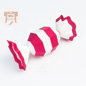 May include: A paper candy with red and white stripes, resembling a wrapped hard candy. The ends are white with a red scalloped edge. The candy is a geometric design, with the text "SVG cut file" in the upper left corner.