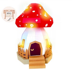 May include: A whimsical paper mushroom house with a red cap dotted with white spots and a white base. The house features a brown door, windows, and a small fence. The image includes the text "SVG cut file".