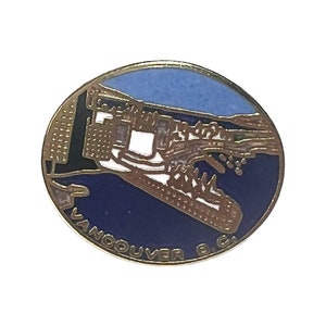 Può includere: Una spilla rotonda in metallo smaltato con una grafica stilizzata dello skyline e del porto di Vancouver, B.C. Il design include un cielo azzurro, acqua blu scuro e sagome di edifici bianchi con il testo VANCOUVER B.C. lungo il bordo inferiore.