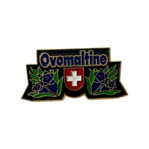 May include: An enamel pin with the word "Ovomaltine" in blue on a black banner. It features a Swiss flag and floral motifs in blue and green, with a gold border.